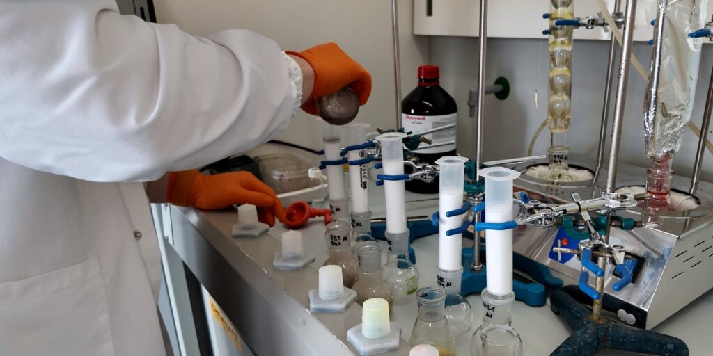 Extraction under a fume hood: orange-gloved hands among columns and laboratory glassware